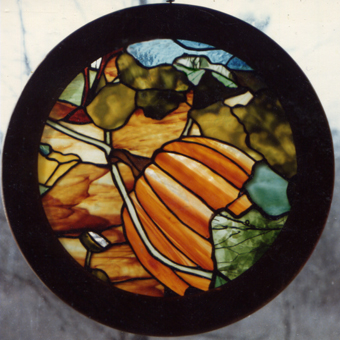 Tiffany style stained glass of a pumpkin in a garden in round wood frame